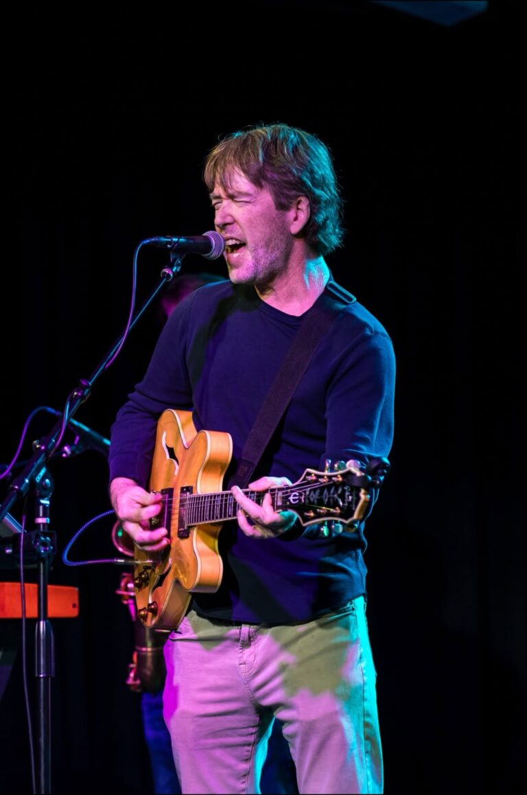 Ron Cook singing lead vocals with acoustic guitar